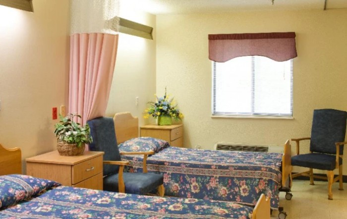 A hospital room with two beds, a chair, and a window with a curtain.