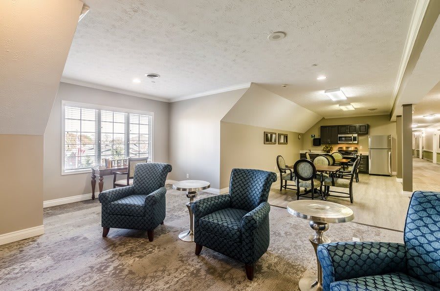 A spacious living room with plush armchairs, a dining area in the background, and natural light streaming through large windows.