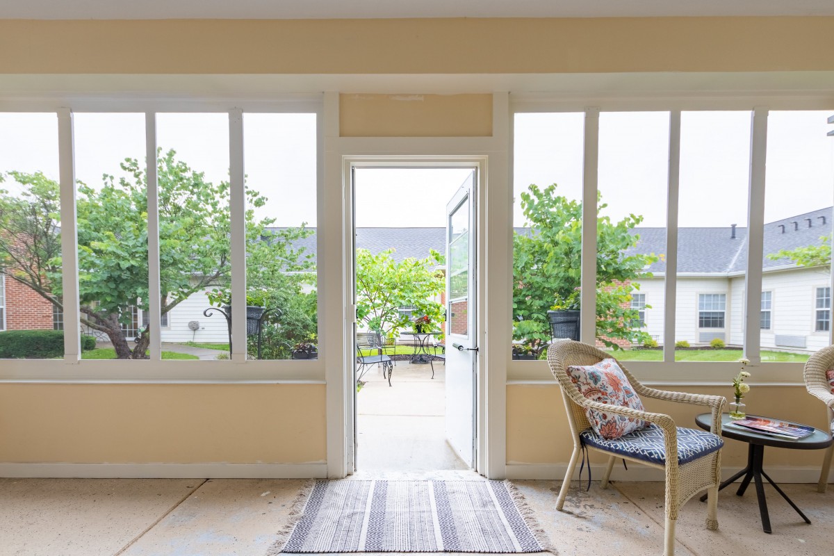 A bright and airy living area with large windows and a door opening to a patio with greenery.