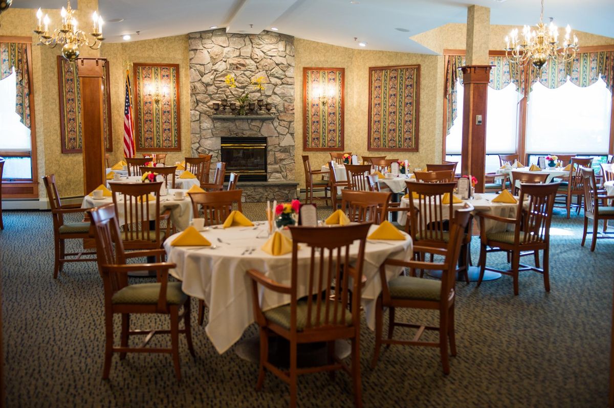 An elegant restaurant dining room featuring round tables and a stone fireplace.