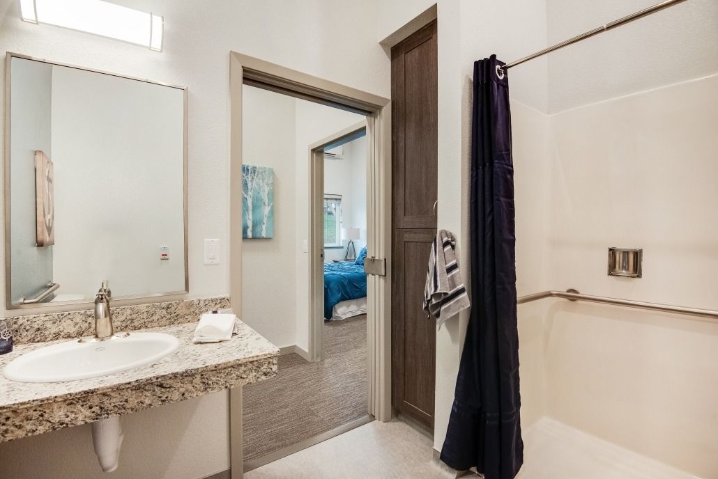 A modern bathroom featuring a sink, mirror, and shower with a view into an adjacent room.