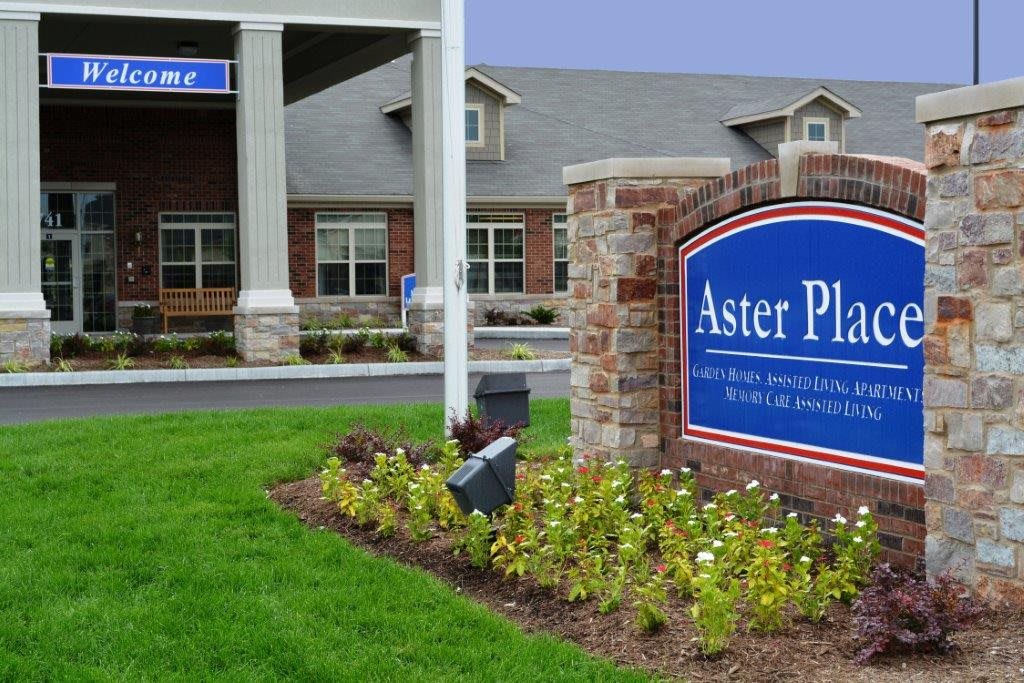 Exterior view of a building with a sign reading 'Aster Place' surrounded by landscaping.