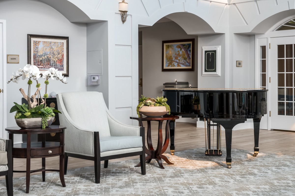 A luxurious lounge area featuring a grand piano, elegant furniture, and framed artwork on the walls.