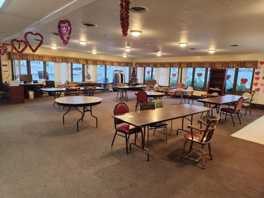 An empty dining hall with tables and chairs arranged, featuring decorative items hanging from the ceiling.