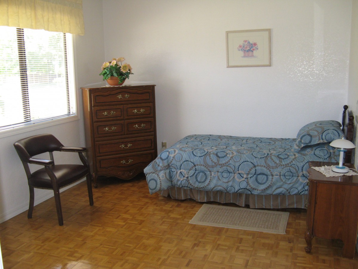 A simple bedroom with a single bed, dresser, and chair by the window.