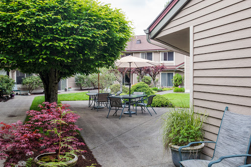 A serene outdoor space featuring a patio with seating, surrounded by vibrant greenery and flowers.