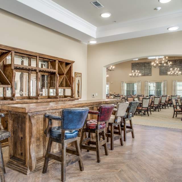 A cozy bar with colorful chairs and a spacious dining area in the background.