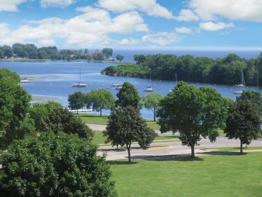 A scenic view of a tranquil lake with sailboats, surrounded by lush green trees and a vibrant blue sky.