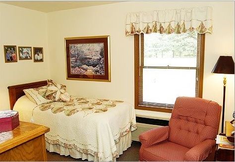 A cozy bedroom with a single bed, an armchair, and wall decorations by a window.