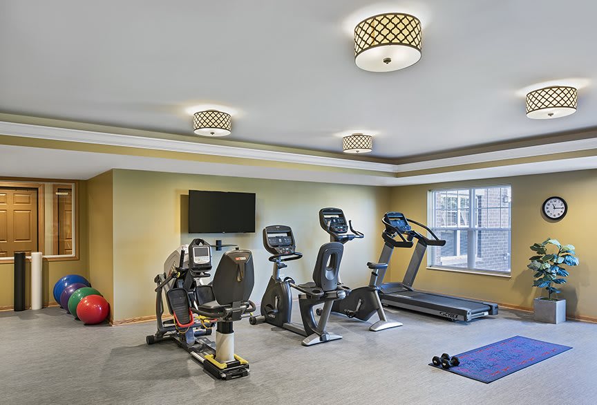 A modern gym room equipped with various exercise machines, including a treadmill, stationary bikes, and an elliptical trainer.