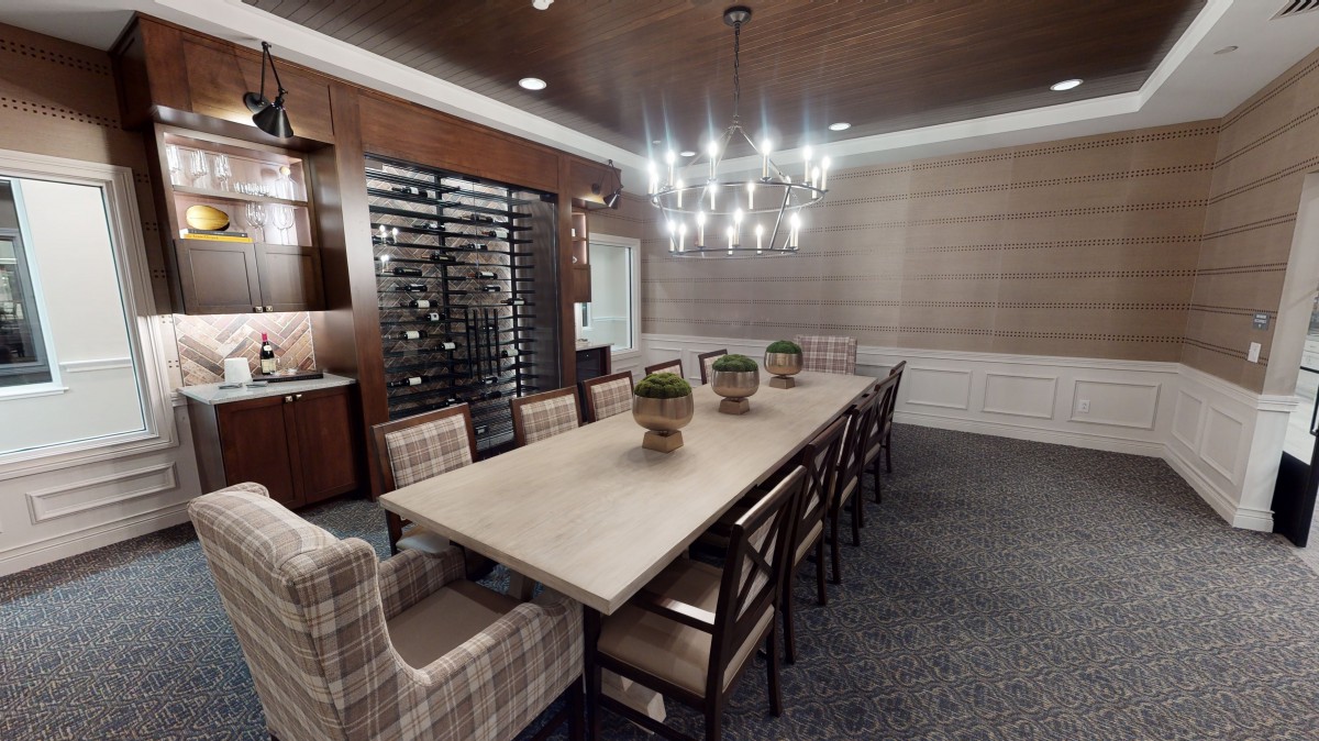 A modern dining room featuring a long table with chairs, a prominent wine rack, and stylish lighting.