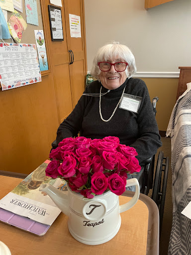 An elderly woman in a wheelchair enjoys a vibrant bouquet of roses in a care facility.