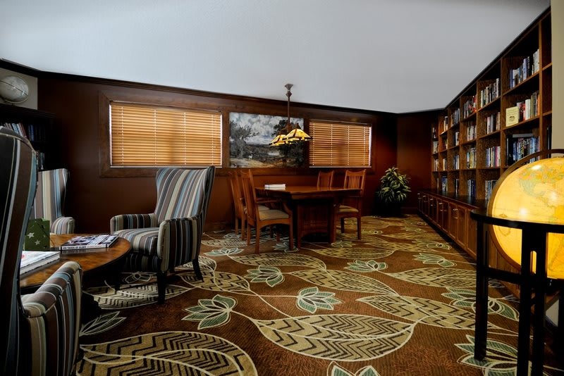 A cozy library reading room with wood paneling, bookshelves, and comfortable furniture.
