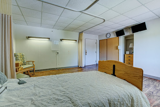A spacious and well-lit hospital room featuring a bed, chair, and storage cabinets.