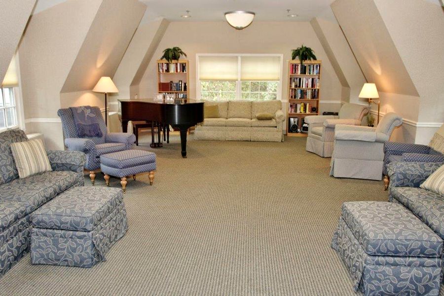 A spacious living room with a grand piano, comfortable seating, bookshelves, and large windows.