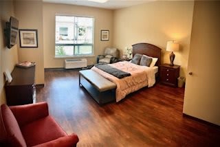 A cozy bedroom with a large bed, hardwood floors, and natural light from a window.