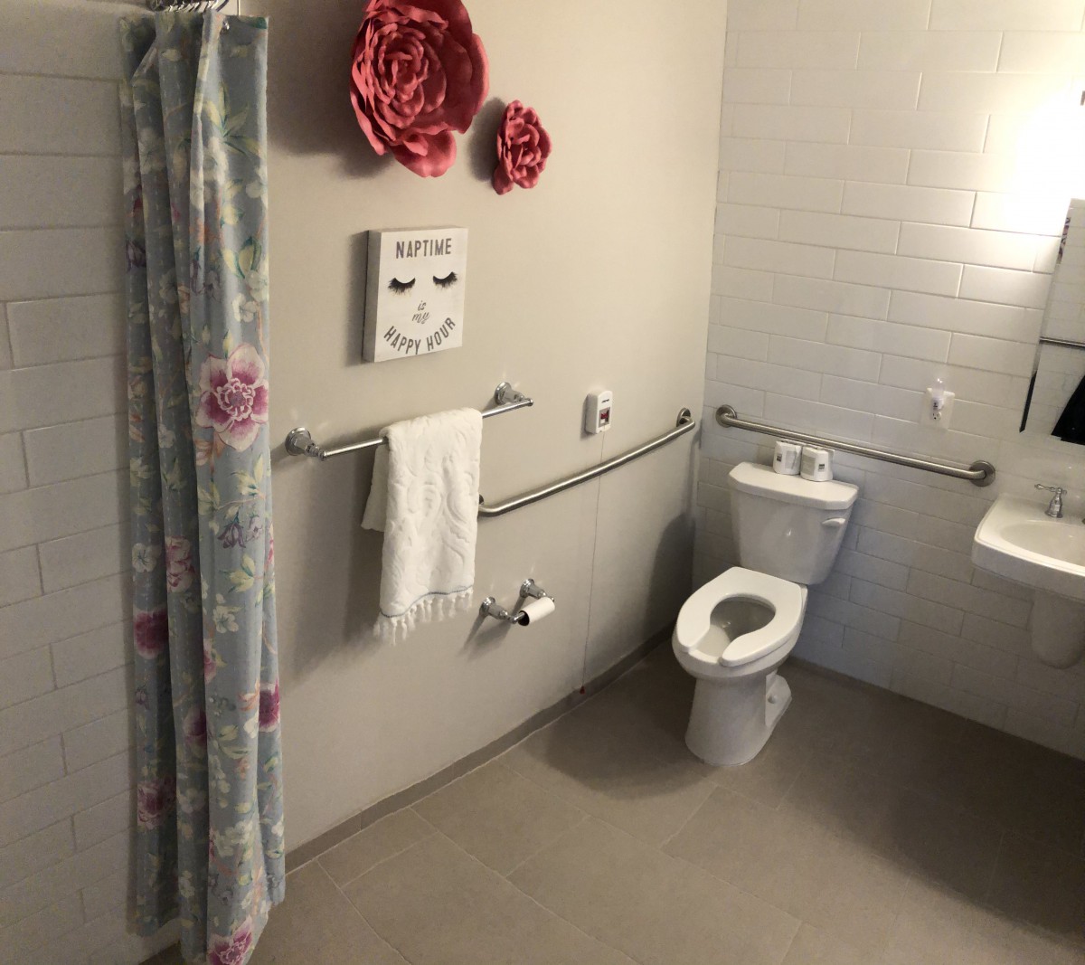 An accessible bathroom with a toilet, shower curtain, and handrails, decorated with wall art and a towel.