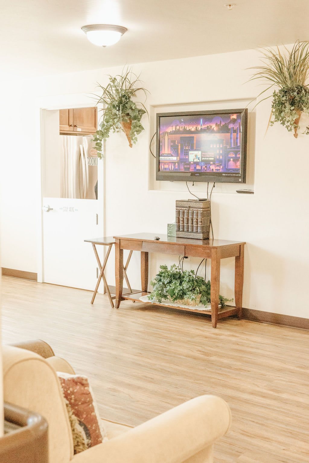 A cozy living room with a wooden table, decorative plants, and a television mounted on the wall.