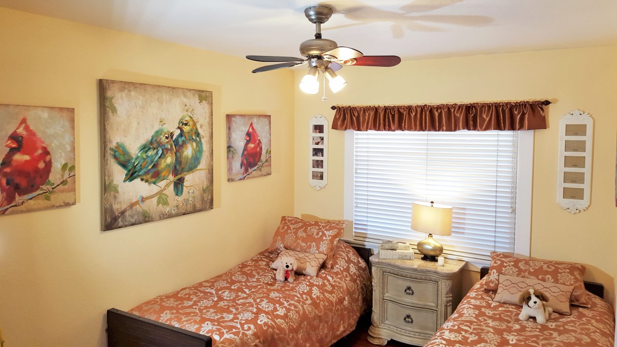 A cozy bedroom with twin beds, bird-themed artwork, and a ceiling fan.
