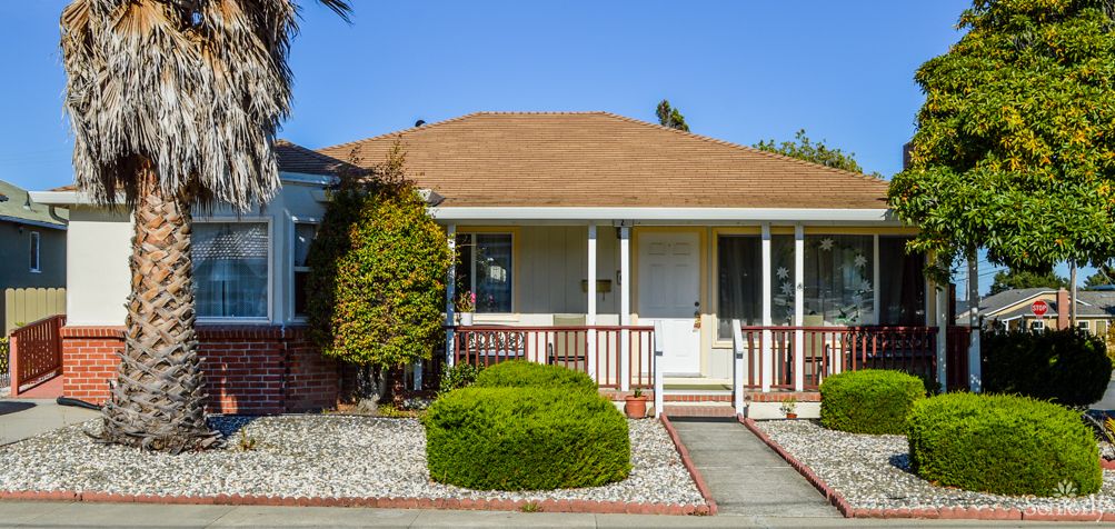 A cozy bungalow with a front porch and landscaped garden on a sunny day.