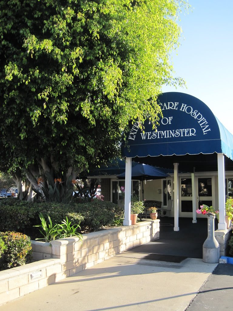 Entrance to a building with an awning labeled 'Administration', surrounded by trees and landscaping.