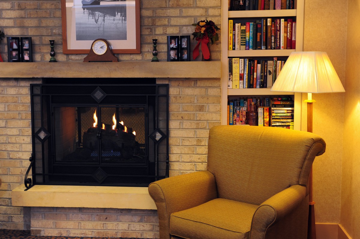 A cozy living room with a fireplace, armchair, and a well-stocked bookshelf.