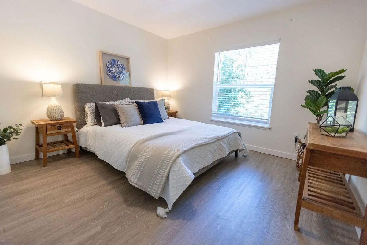 A modern bedroom with a neatly made bed, decorated with cushions and throws, and illuminated by bedside lamps.