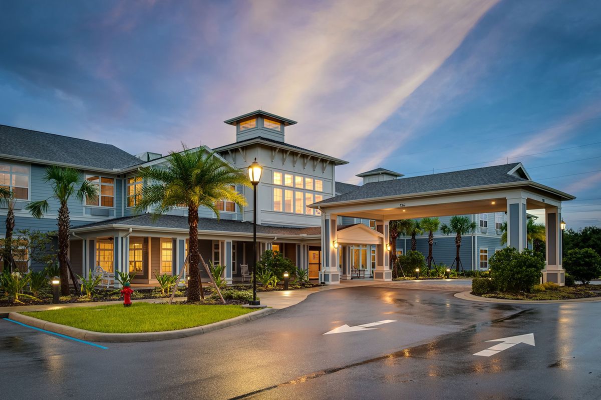 An elegant hotel with modern architecture, illuminated in the evening, surrounded by palm trees.