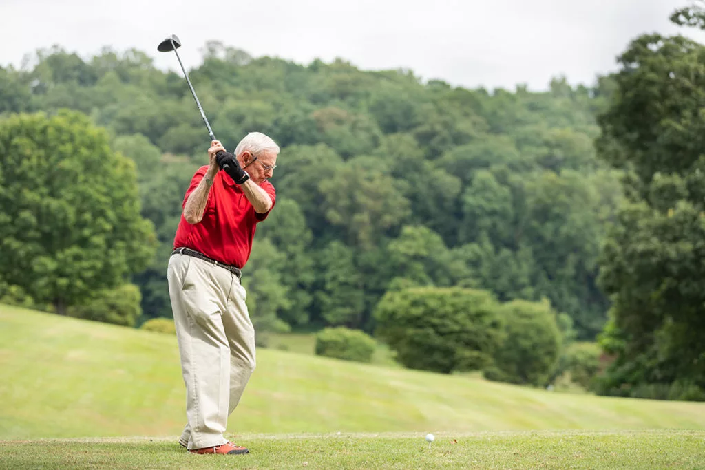 A senior golfer swinging a club on a lush green course.