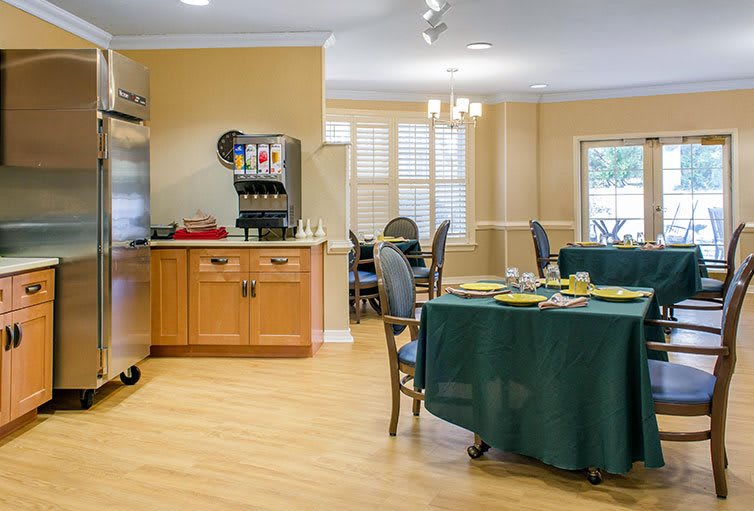 A well-lit dining room with neatly set tables and a kitchen area.
