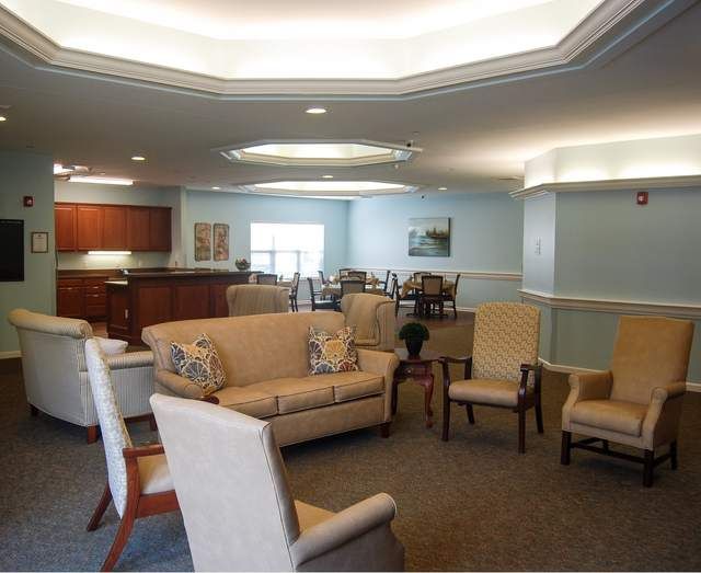 A comfortable living room with sofas and chairs arranged around a central table, featuring elegant lighting.