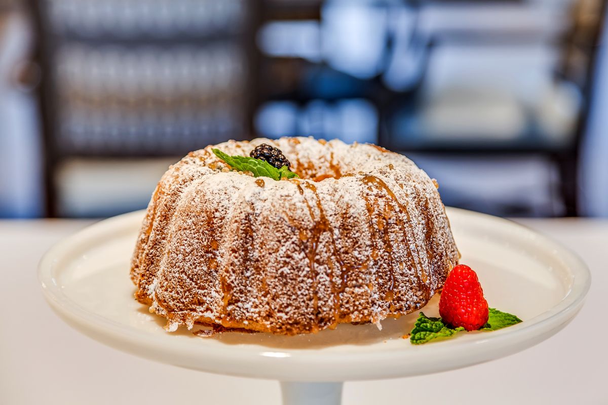 A delicious bundt cake dusted with powdered sugar, garnished with raspberries and mint leaves on a cake stand.