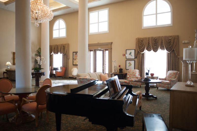 A luxurious living room featuring a grand piano, elegant furniture, and large windows with high ceilings.