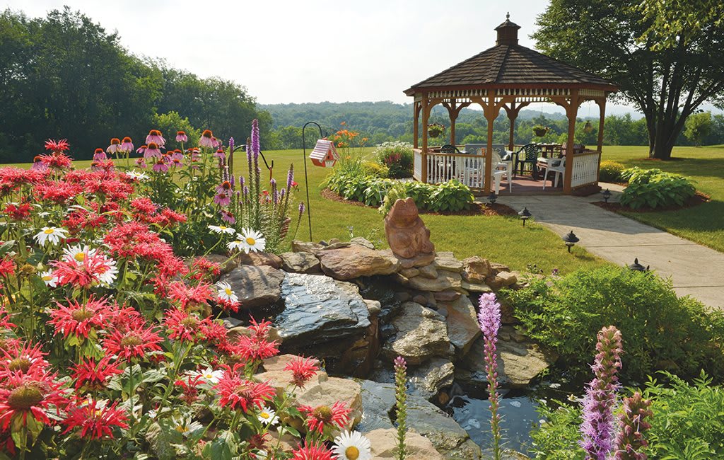 A picturesque garden with vibrant flowers and a tranquil pond, featuring a wooden gazebo in the background.