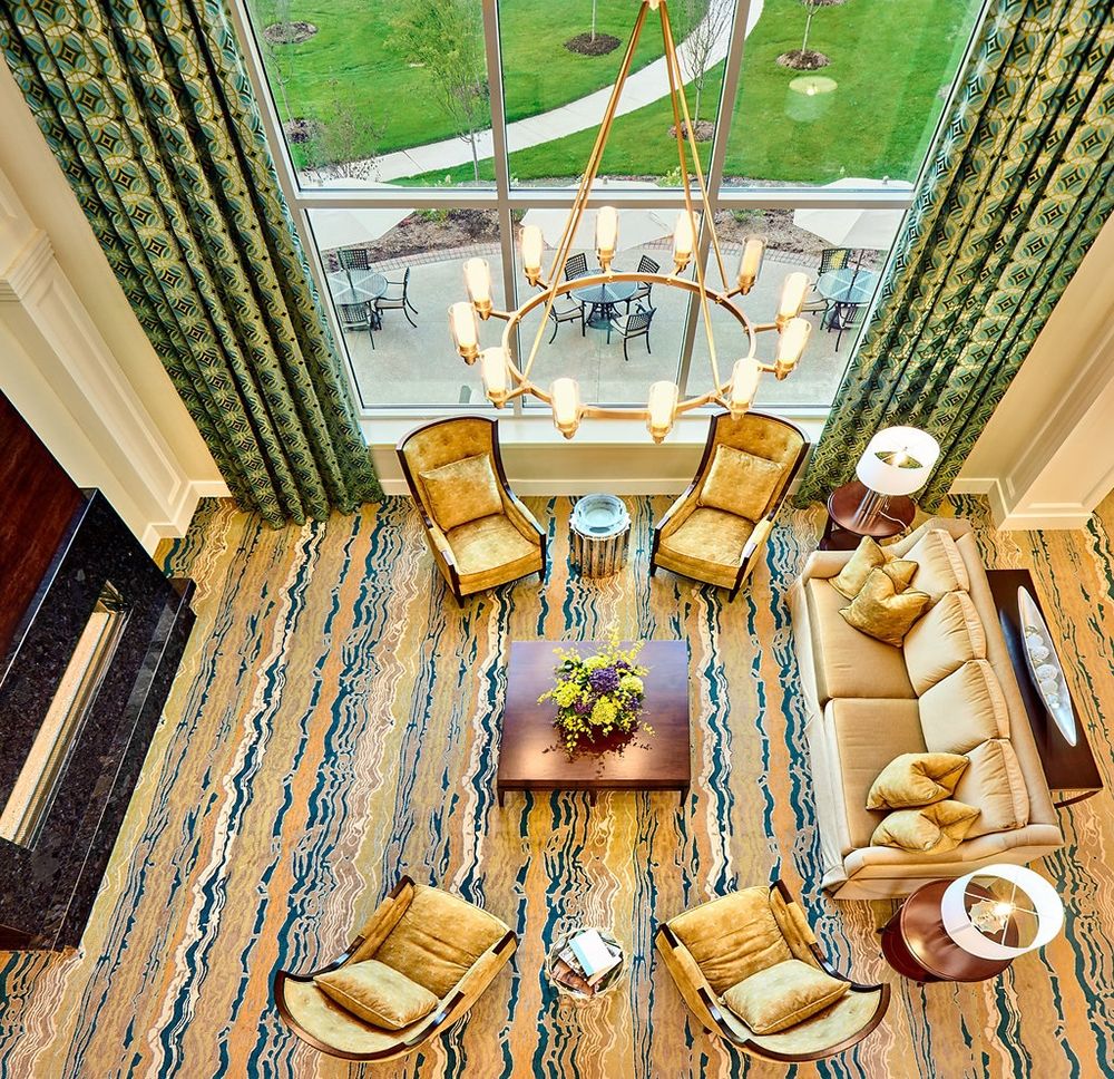 A beautifully designed living room with a cozy seating arrangement, seen from an aerial perspective. The room features a stylish chandelier, large windows, and modern furniture.
