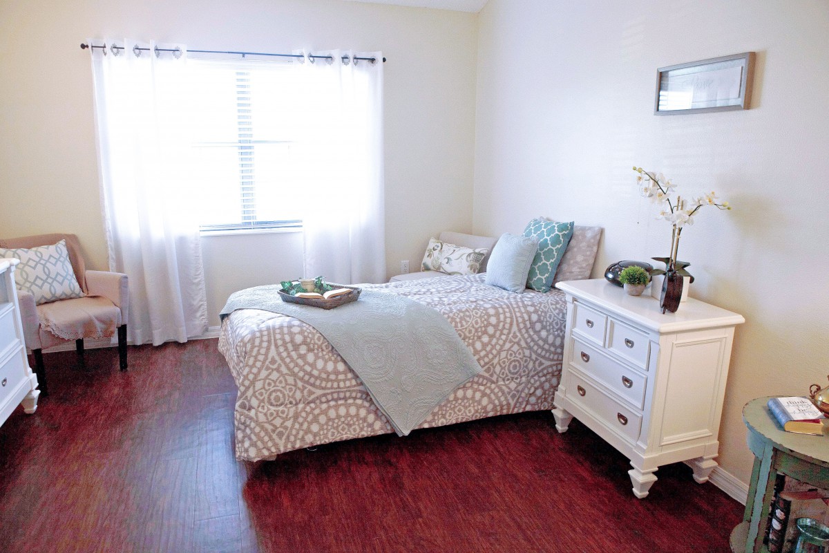 A cozy and well-lit bedroom featuring a bed with patterned bedding and a white nightstand.