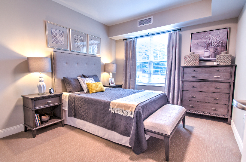 A modern bedroom with a grey color scheme, featuring a neatly made bed, bedside tables, and a window with curtains.
