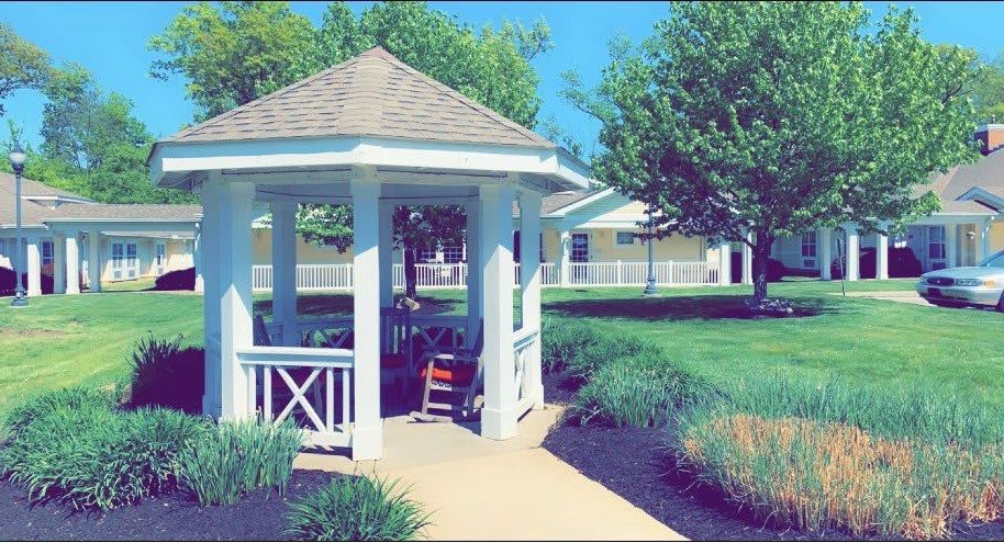 A quaint gazebo surrounded by lush greenery on a sunny day.
