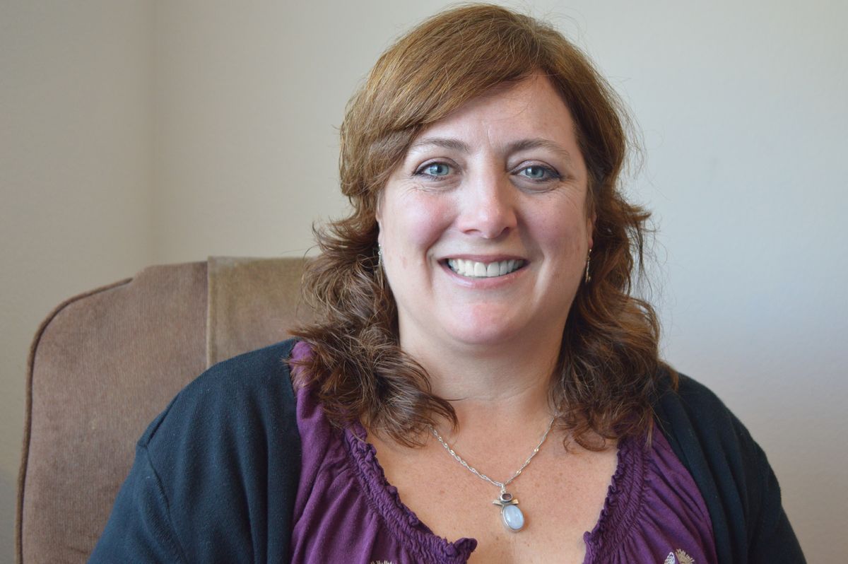 A smiling woman indoors, sitting on a chair.