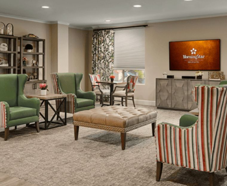 A cozy living room featuring comfortable armchairs, a central ottoman, and a TV area.