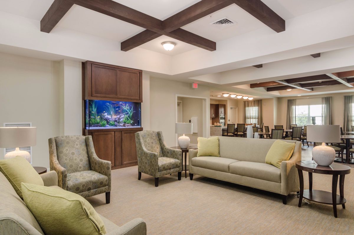 A modern living room featuring sofas, armchairs, an aquarium, and wooden ceiling beams, all in a neutral color scheme.
