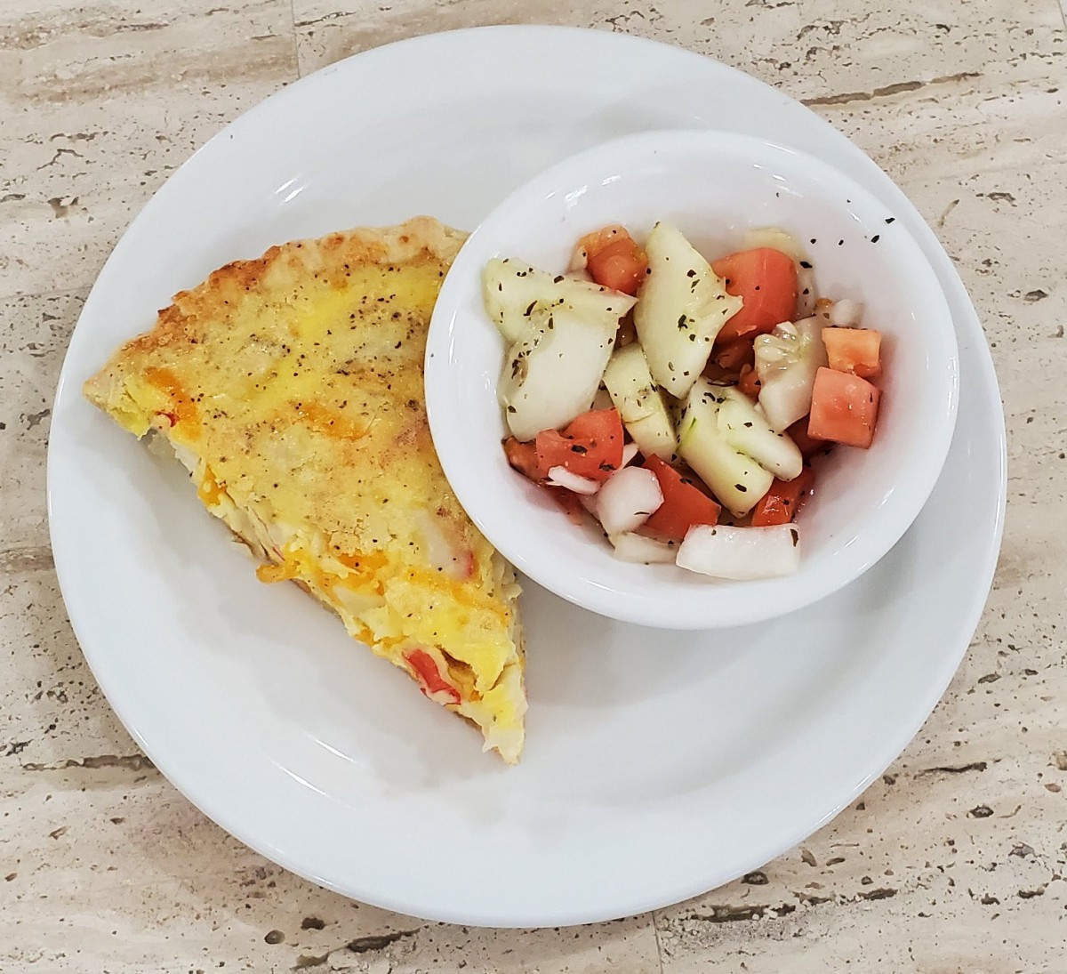 A plate with a slice of omelette and a bowl of vegetable salad.