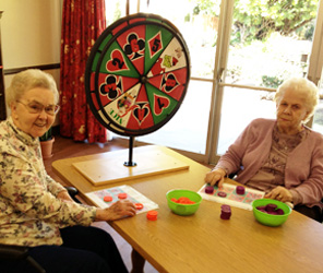 Two elderly women enjoying a game together with a colorful spinning wheel in a bright indoor setting.