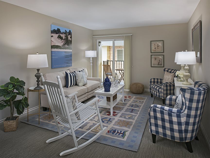A cozy living room with a rocking chair, sofa, patterned armchairs, lamps, and decorative elements.