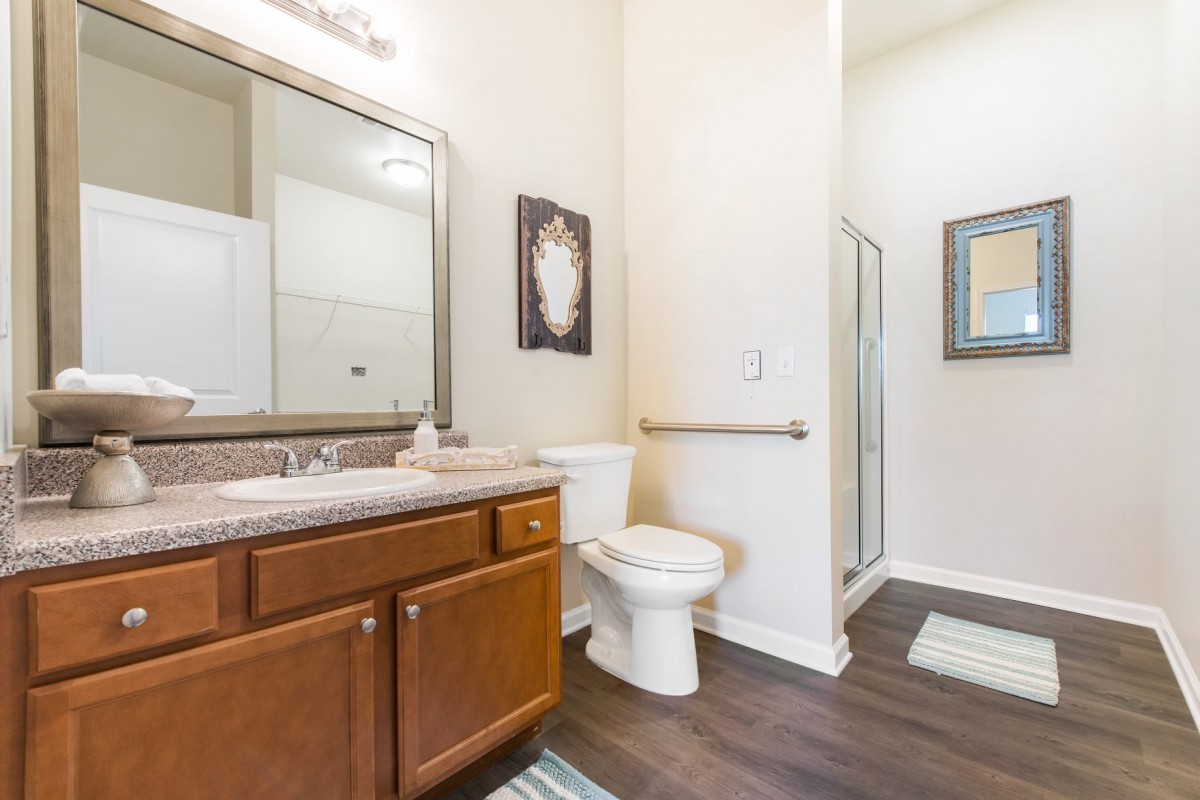 A modern bathroom featuring a wooden cabinet, toilet, sink with mirror, and a glass-enclosed shower.