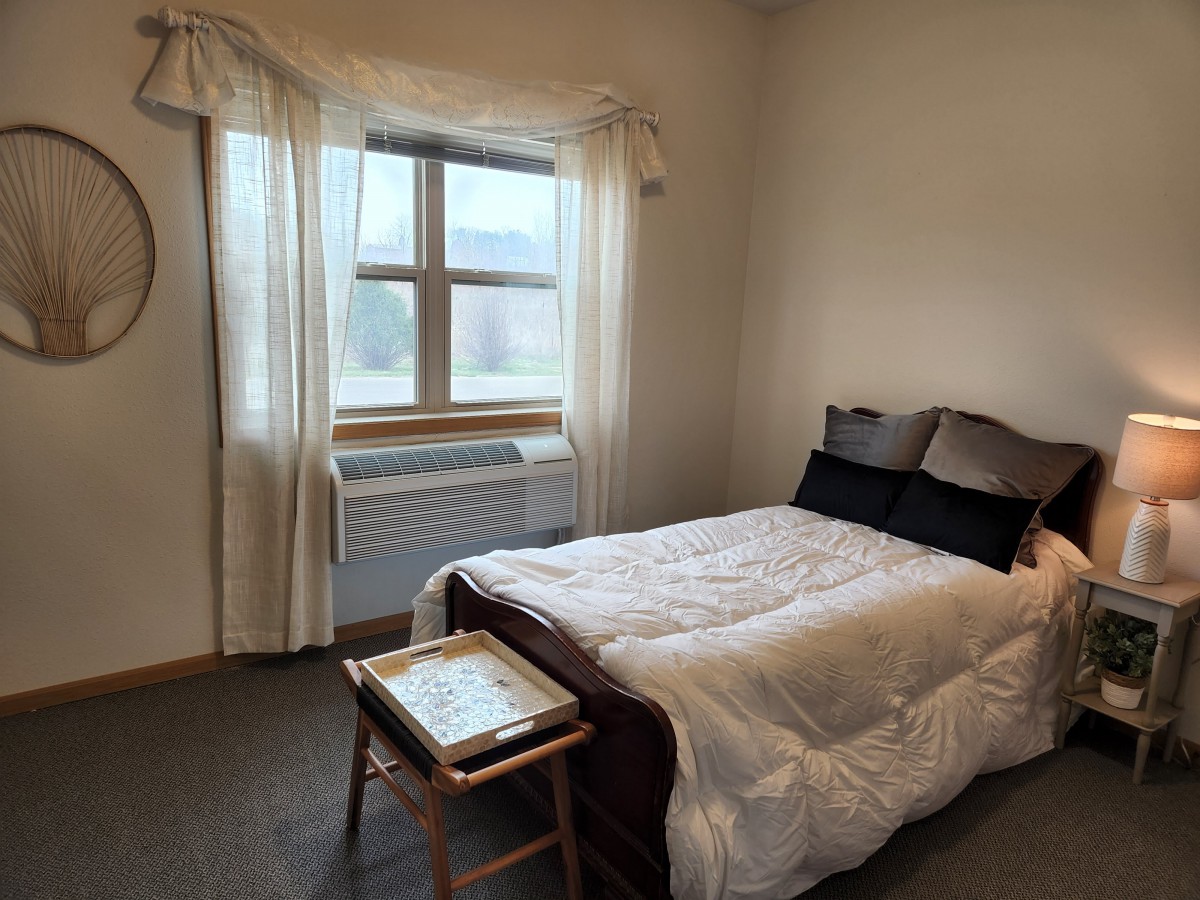 A minimalist bedroom with a neatly made bed next to a window and nightstand.