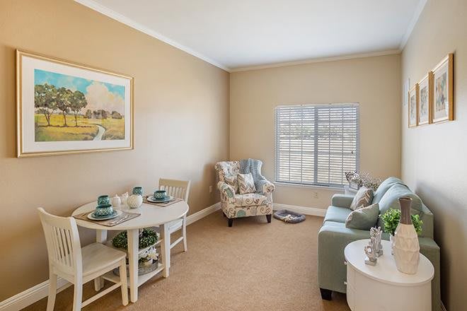A cozy living room with neutral tones, featuring a comfortable armchair, sofa, and a small dining area.
