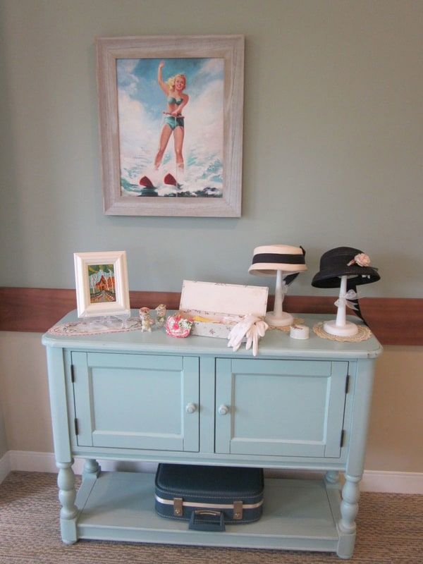 A vintage-style cabinet with nautical-themed decor and elegant hats displayed on top.