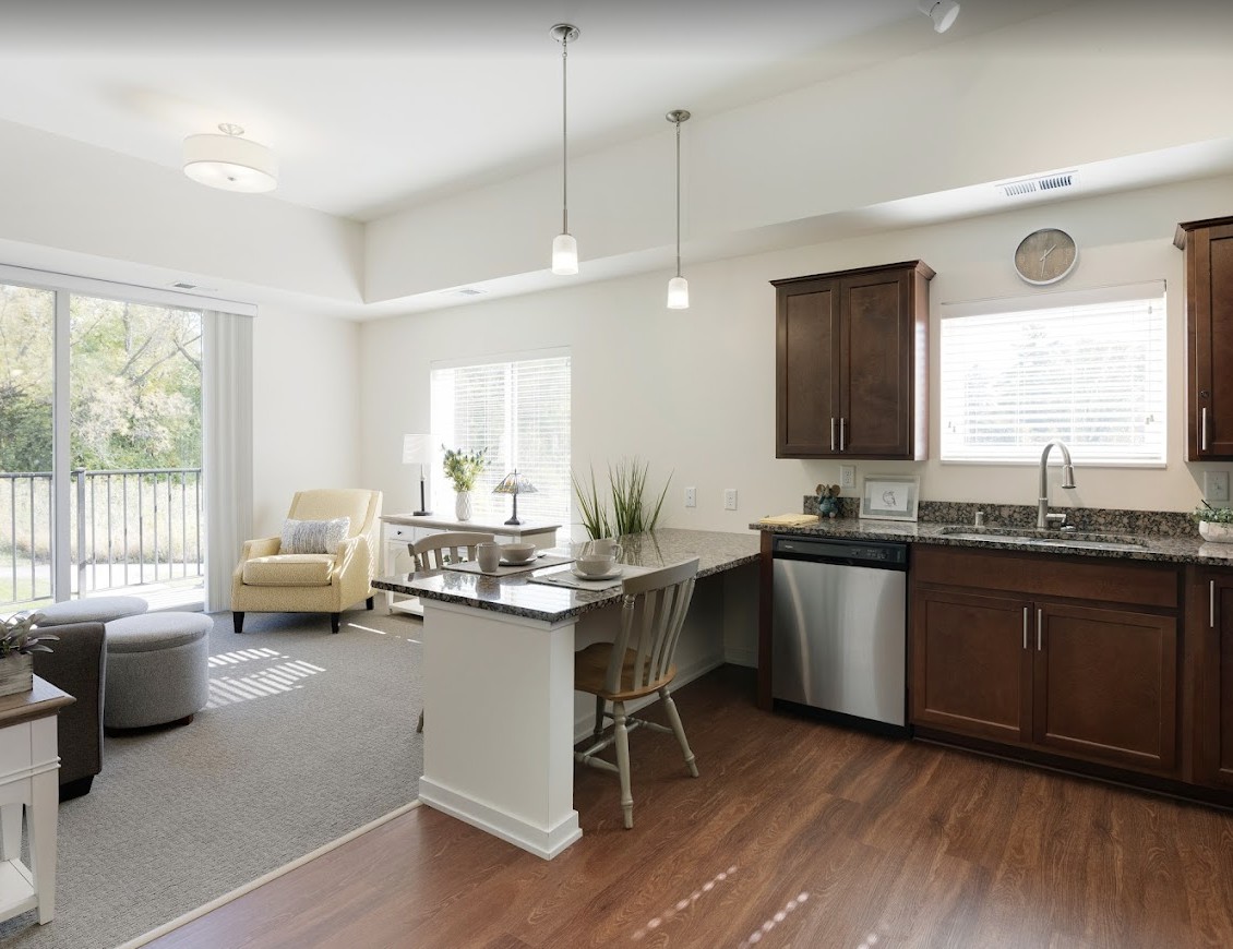 A modern open-concept kitchen and living room with wood flooring, warm natural lighting, and contemporary furnishings.