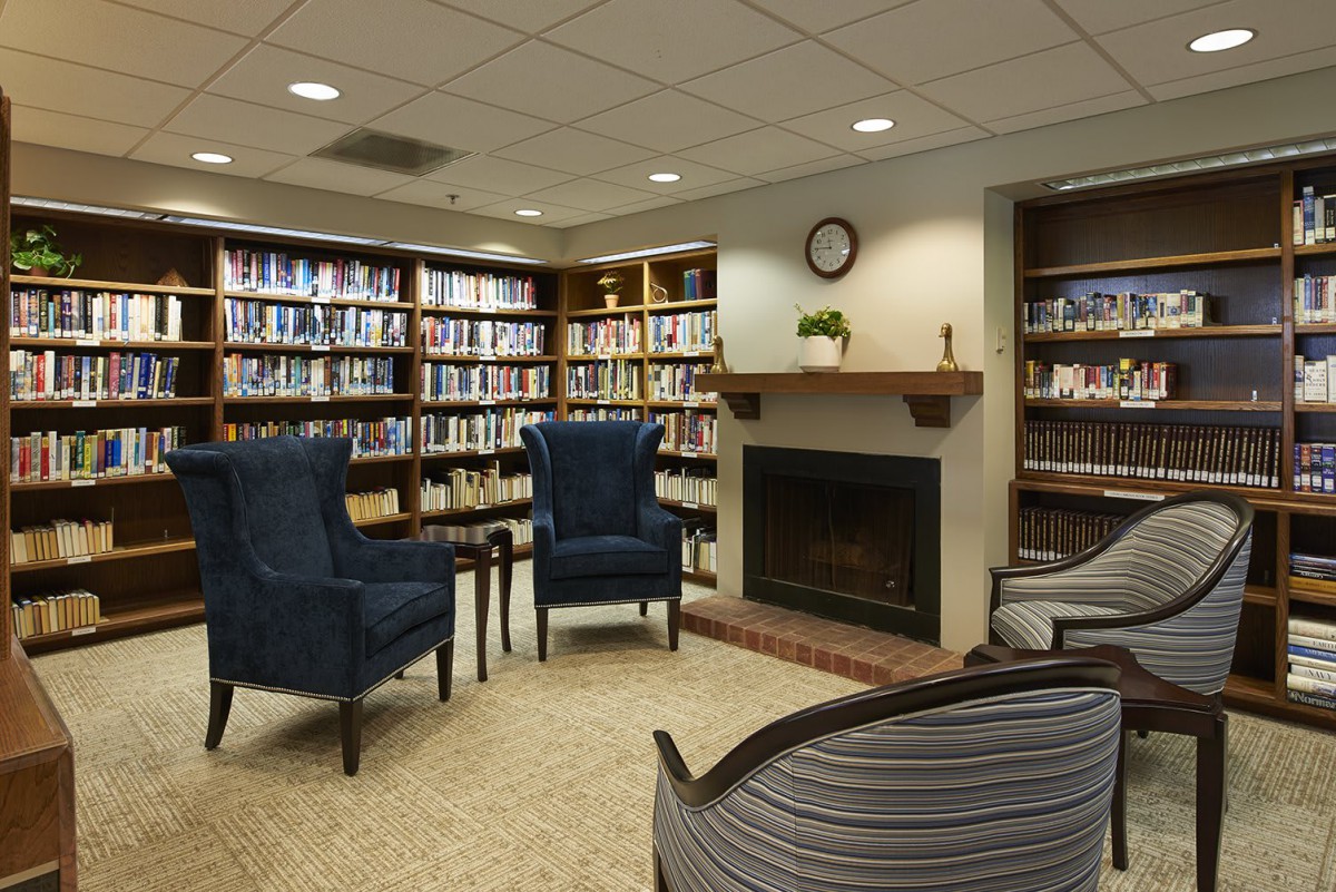 A cozy library reading area with bookshelves, a fireplace, and comfortable chairs.
